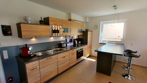 Moderni keittiö, jossa on puiset kaapit, sisäänrakennettu uuni ja kahvinkeitin.