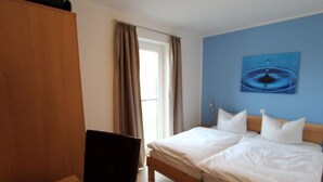 Hotellihuone, jossa on sänky, tuoli, työpöytä ja ikkuna, jossa on verhot.