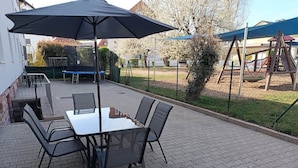 Un patio exterior con una mesa y sillas, una parrilla y un columpio al fondo.