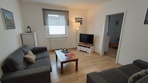 Una sala de estar con dos sofás, una mesa de centro, un televisor y un ventanal.
