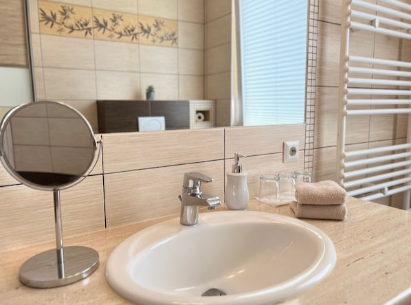 A bathroom with a round mirror, a sink, a towel rack, and a decorative tile backsplash. - Apartment 5 no. First floor - Villa Trautes Heim (Heringsdorf)