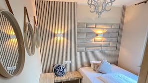 A bedroom with a bed, a bedside table, a decorative wall panel, and a wall-mounted light fixture. - Apartment 5 no. First floor - Villa Trautes Heim (Heringsdorf)