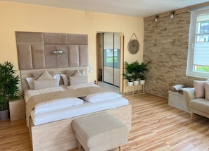 A bedroom with a large bed, a sofa, a stone wall, and a window. - Apartment 5 no. First floor - Villa Trautes Heim (Heringsdorf)
