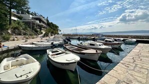 Un puerto deportivo con varias embarcaciones amarradas, un sendero de piedra y un edificio con balcones que dan al agua.