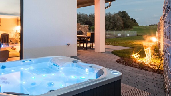 A hot tub with multiple jets, a patio area with outdoor furniture, and a fire feature.