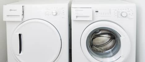 Two front-loading washing machines in a corner of a room with a tiled floor and a white wall.