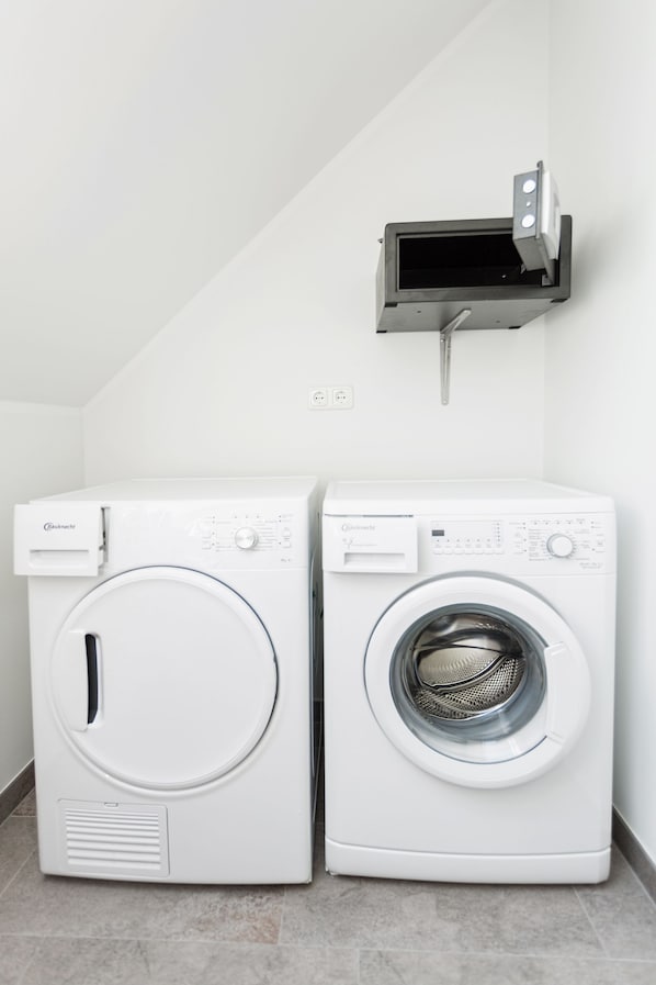 Two front-loading washing machines in a corner of a room with a tiled floor and a white wall.