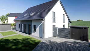 A modern single-story house with a sloped roof, a small balcony, and a gated driveway.