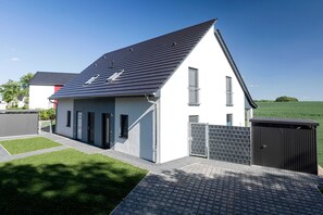 A modern single-story house with a sloped roof, a small balcony, and a gated driveway.