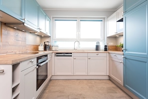 A modern kitchen with white cabinets, a wooden countertop, a dishwasher, and a window above the sink.