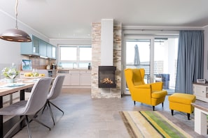 A modern living room with a fireplace, a dining area, and a kitchen in the background.
