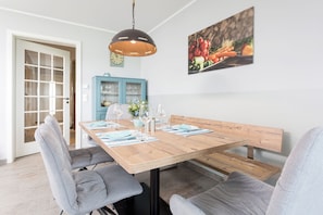 A dining area with a wooden table set for four, grey upholstered chairs, a blue cabinet, and a wall-mounted picture of vegetables.