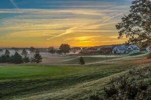 A rural landscape with a sunset, houses, and a grassy field.