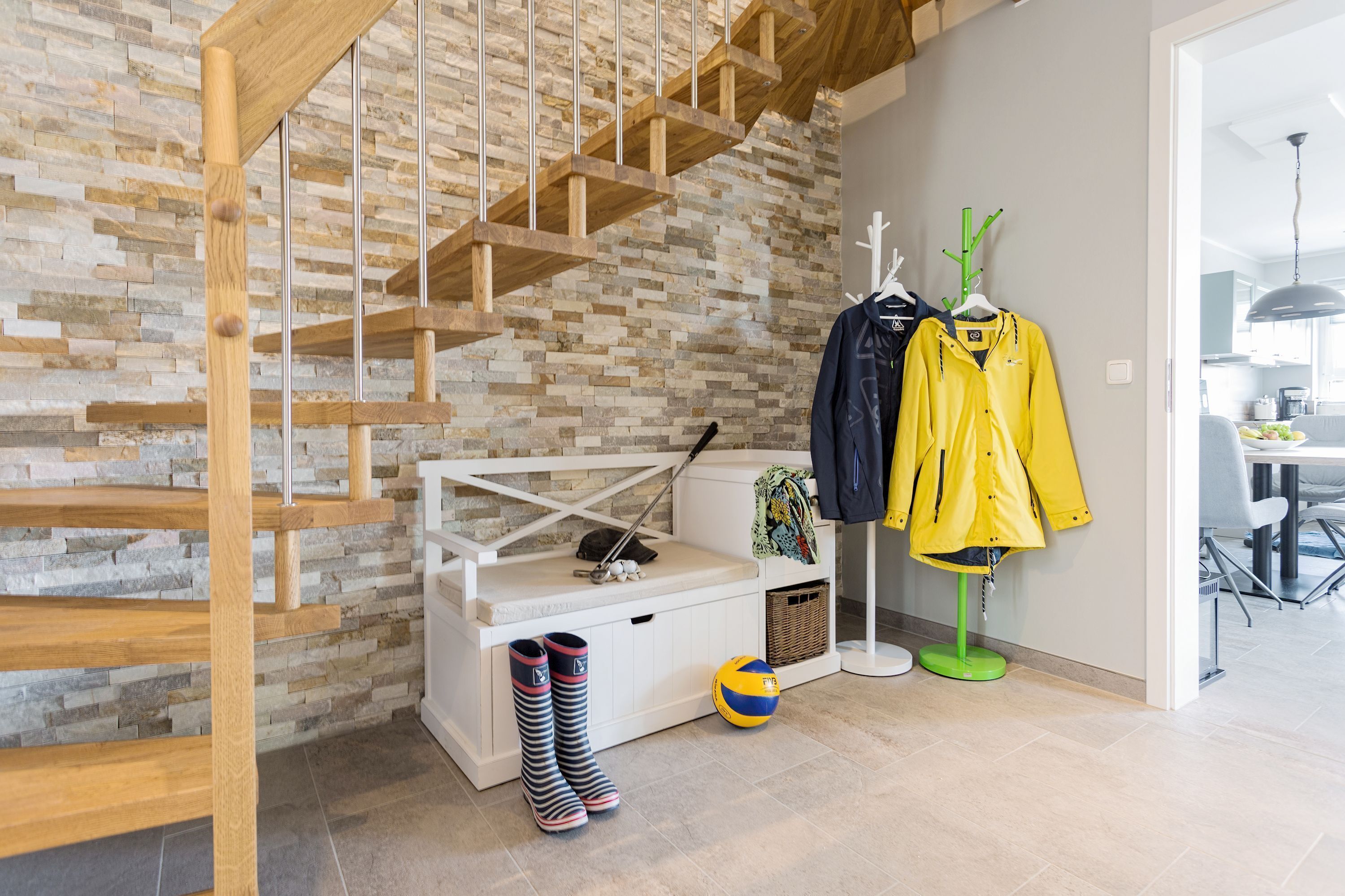 A staircase with a wooden finish, a white bench with a basket, and a volleyball on the floor.