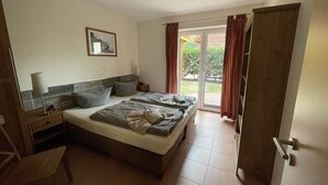 Ein Schlafzimmer mit einem Bett, einem Nachttisch, einer Lampe, einem Sessel und einer Glastür, die auf einen Balkon führt.