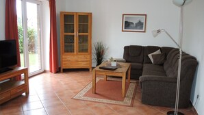Ein Wohnzimmer mit einer Couch, einem Couchtisch, einem Fernseher auf einem Schrank, einem Schrank und einer Stehlampe.