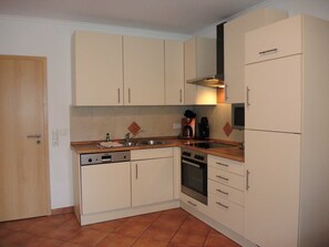 Una cucina compatta con mobili bianchi, lavastoviglie, forno e frigorifero.