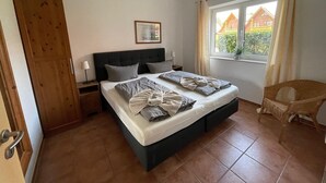 Ein Schlafzimmer mit einem großen Bett, einem Holzschrank, einem Nachttisch, einem Fenster mit Vorhängen und Blick auf Gebäude.