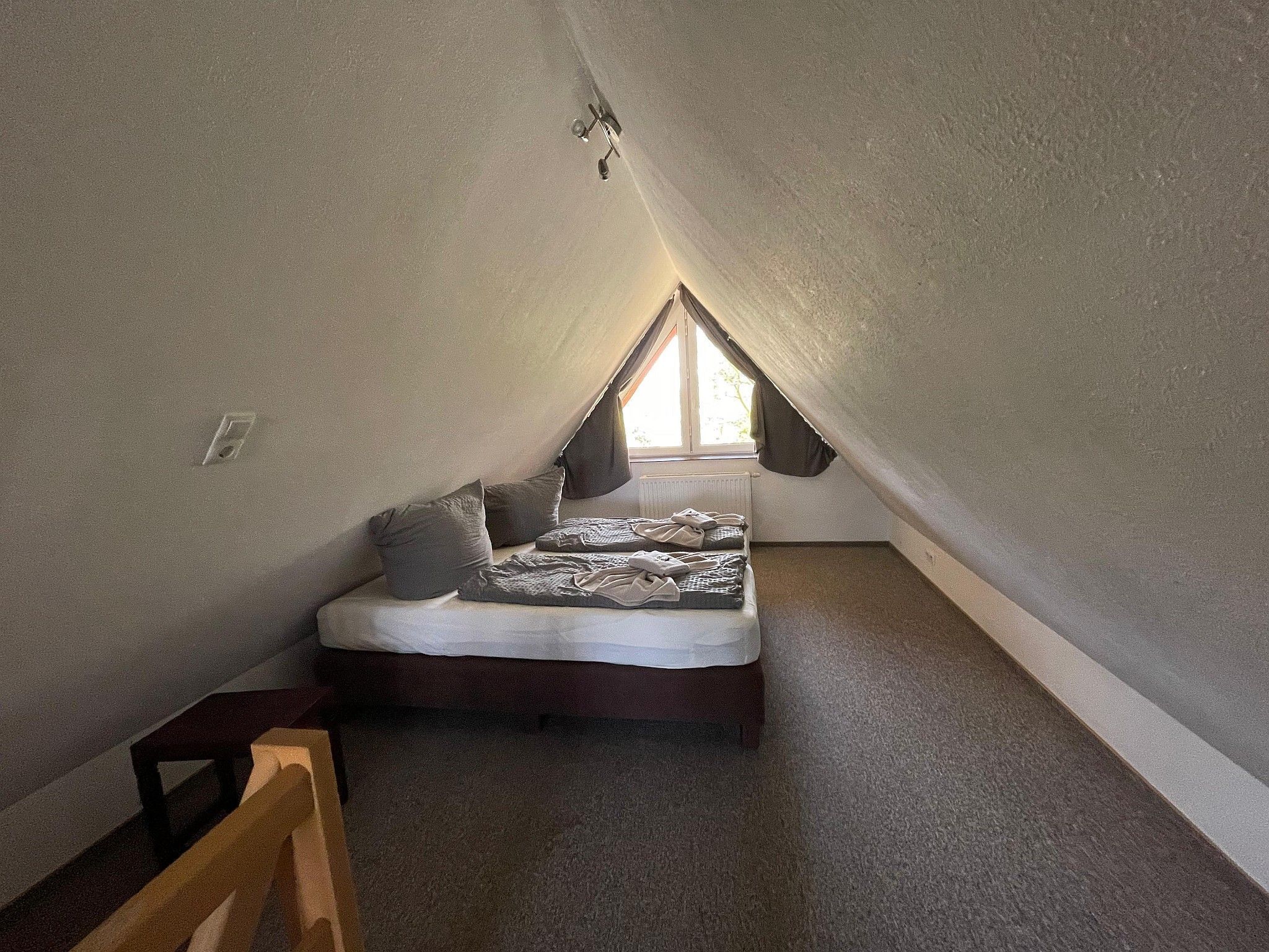 A small, cozy attic bedroom with a sloped ceiling, a single bed, and a window providing natural light.