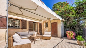 Un área de estar al aire libre con techo, muebles de mimbre y una mesa, una planta en maceta y una puerta de madera.