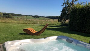 A hot tub with a wooden chair leaning against it, surrounded by a grassy area and a fence. - House BELLEVUE upper floor (Göhren-Lebbin)