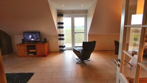 A living room with a television, a chair, and a view through a glass door. - House BELLEVUE upper floor (Göhren-Lebbin)