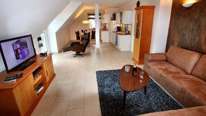 A modern living room with a TV, sofa, and coffee table. A kitchen is visible in the background. - House BELLEVUE upper floor (Göhren-Lebbin)