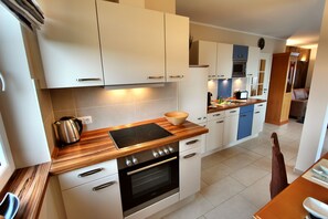 Uma cozinha moderna com armários brancos, bancada de madeira, forno embutido e micro-ondas.
