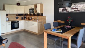 A modern kitchen with white cabinets, a wooden countertop, and a dining area with a wooden table and chairs. - Villa Grande / Luxus-EG-Fewo ENJOY - Villa Grande / Luxus-EG-Fewo ENJOY (WE 2) (Göhren-Lebbin)