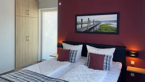 A bedroom with a bed, a wardrobe, a picture on the wall, and a window with blinds. - Villa Grande / Luxus-EG-Fewo ENJOY - Villa Grande / Luxus-EG-Fewo ENJOY (WE 2) (Göhren-Lebbin)