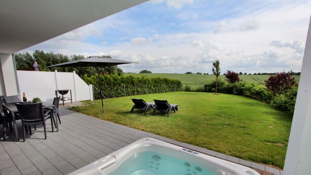 A patio with a hot tub, outdoor furniture, and a view of a grassy field. - Villa Grande / Luxus-EG-Fewo ENJOY - Villa Grande / Luxus-EG-Fewo ENJOY (WE 2) (Göhren-Lebbin)