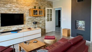 A modern living room with a stone wall, a flat-screen TV, a wooden cabinet, a fireplace, and a red leather sofa. - Villa Grande / Luxus-EG-Fewo ENJOY - Villa Grande / Luxus-EG-Fewo ENJOY (WE 2) (Göhren-Lebbin)