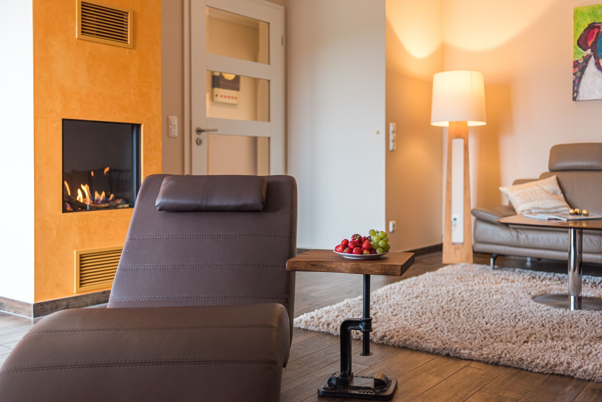 A modern living room with a leather sofa, a small table with fruit, a standing lamp, and a fireplace.