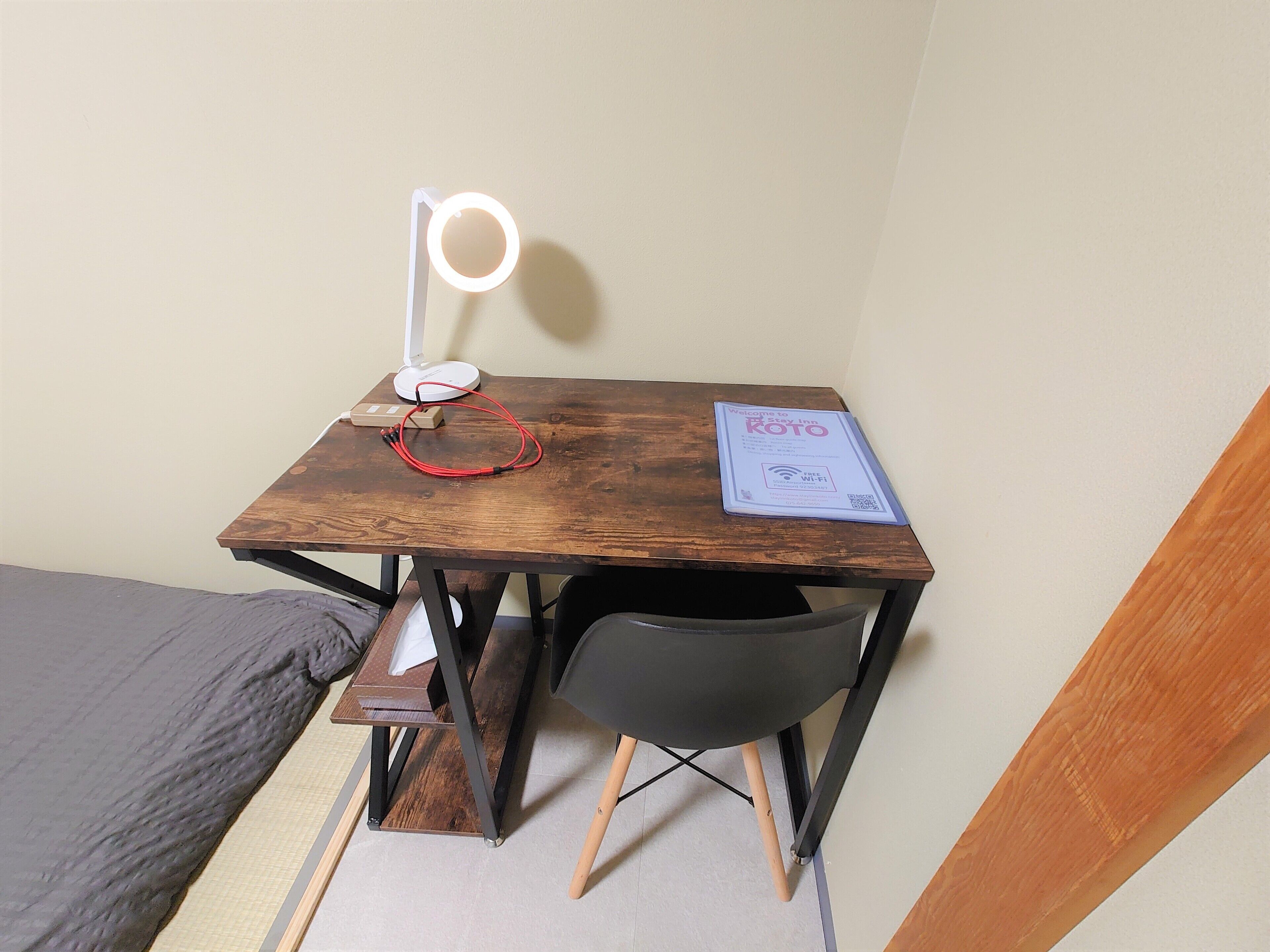A small wooden desk with a ring light, a power strip, and a welcome sign for Koto Inn.