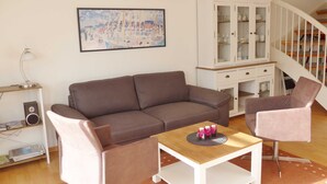 Un salon avec un canapé marron, un fauteuil rose, une table basse en bois, un meuble blanc et un tableau accroché au mur.