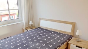Un lit avec une couvre-lit à motifs, une tête de lit en bois, une table de chevet avec une lampe et une fenêtre avec des rideaux.