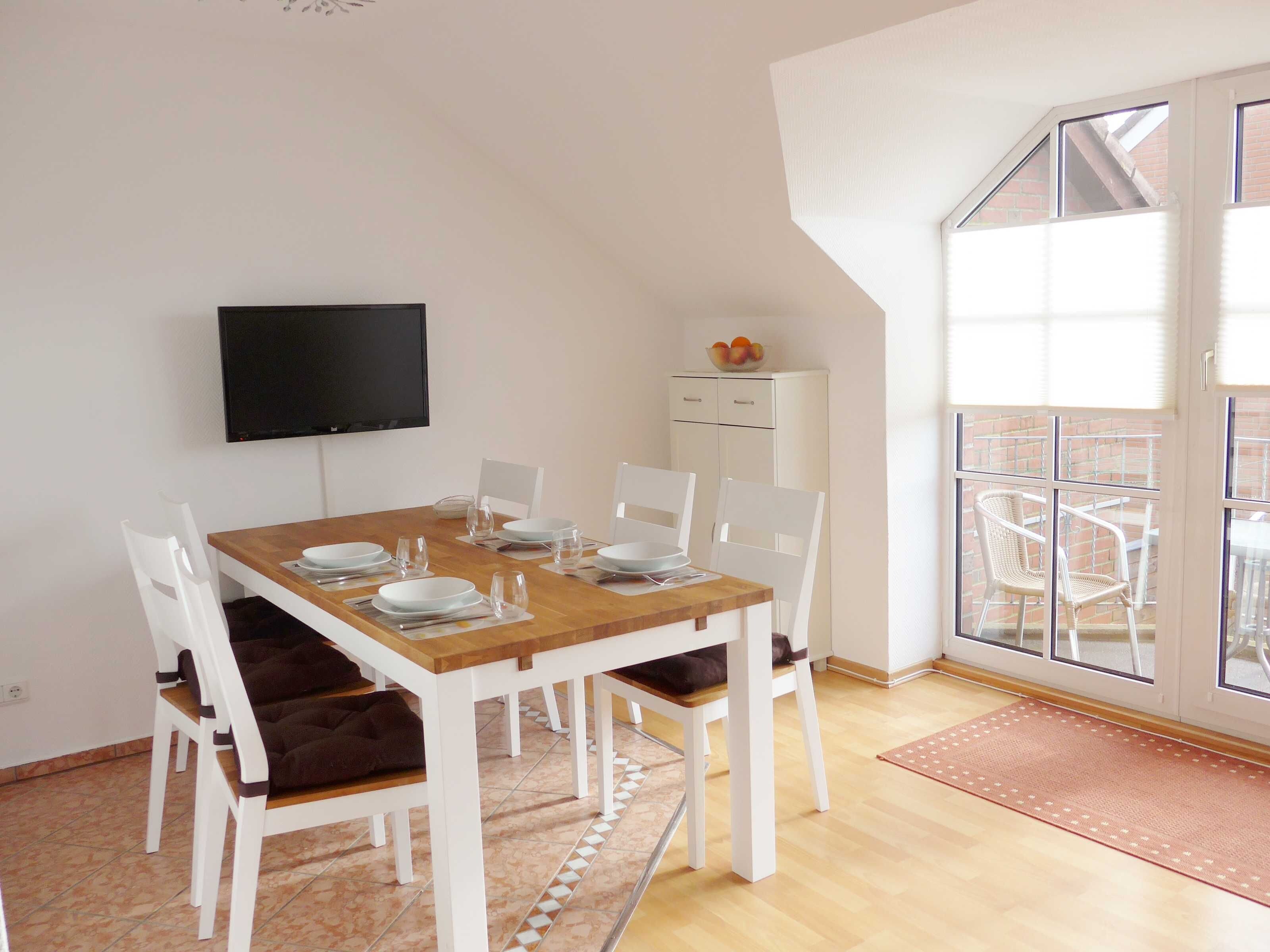 A dining area with a wooden table, white chairs, a TV, and a view of the outside.
