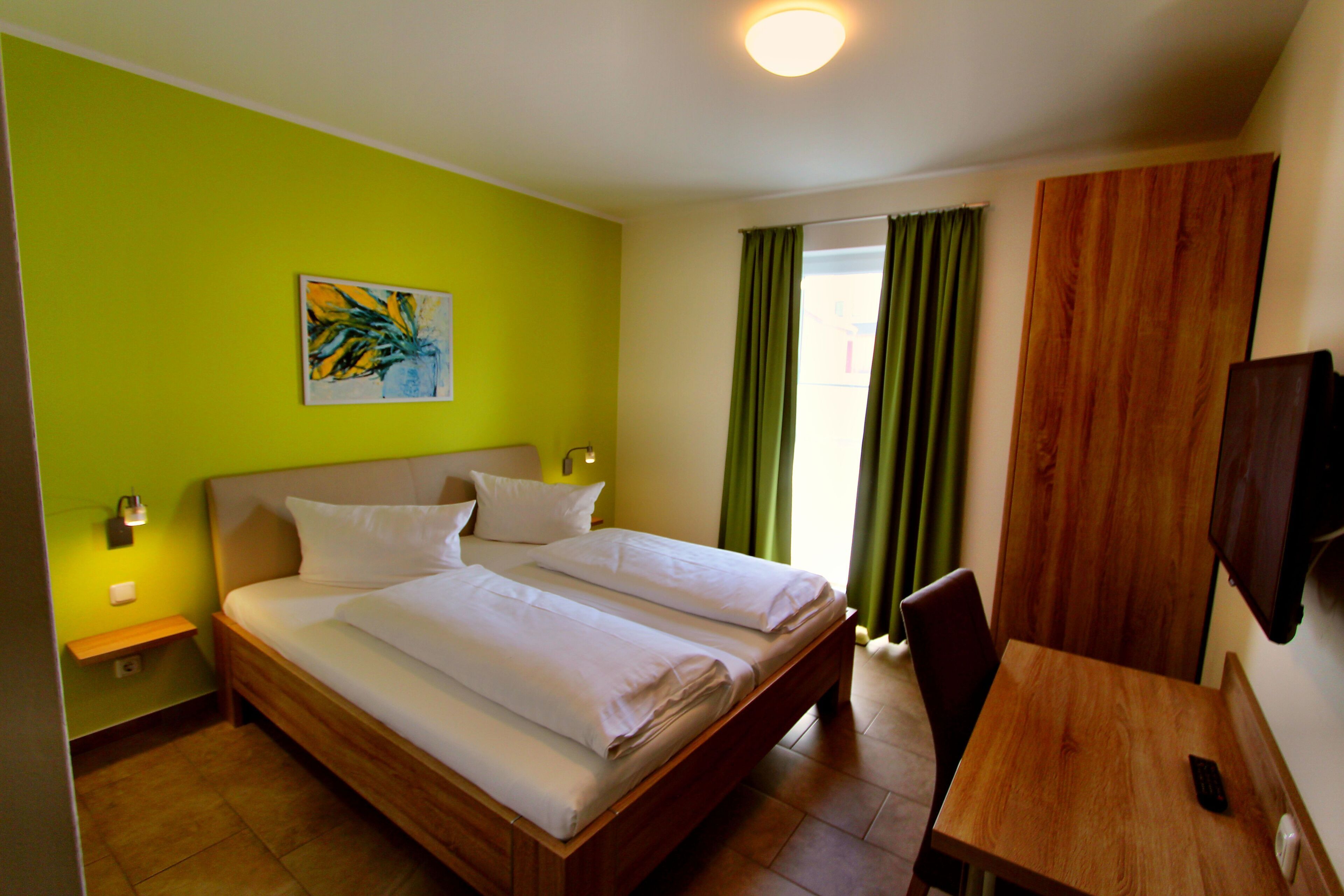 Une chambre d’hôtel avec un lit, un bureau, une chaise, une télévision et un tableau au mur.