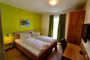 A hotel room with a bed, a desk, a chair, a TV, and a painting on the wall.