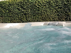 Una vasca idromassaggio con acqua che schizza, circondata da un siepe.