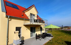 A two-story building with a red roof, a balcony, and a patio area with outdoor furniture.