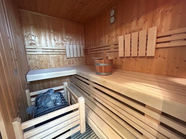 A sauna with wooden walls and benches, a wooden bench with a metal frame, and a small wooden bucket.