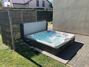 Ein Whirlpool in einem Garten mit Holzzaun, gepflasterter Terrasse und einem Haus im Hintergrund.