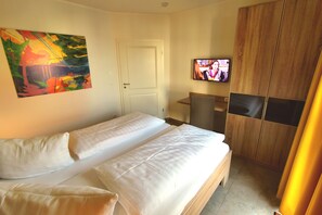 A hotel room with a bed, a TV, a painting, and a wardrobe.