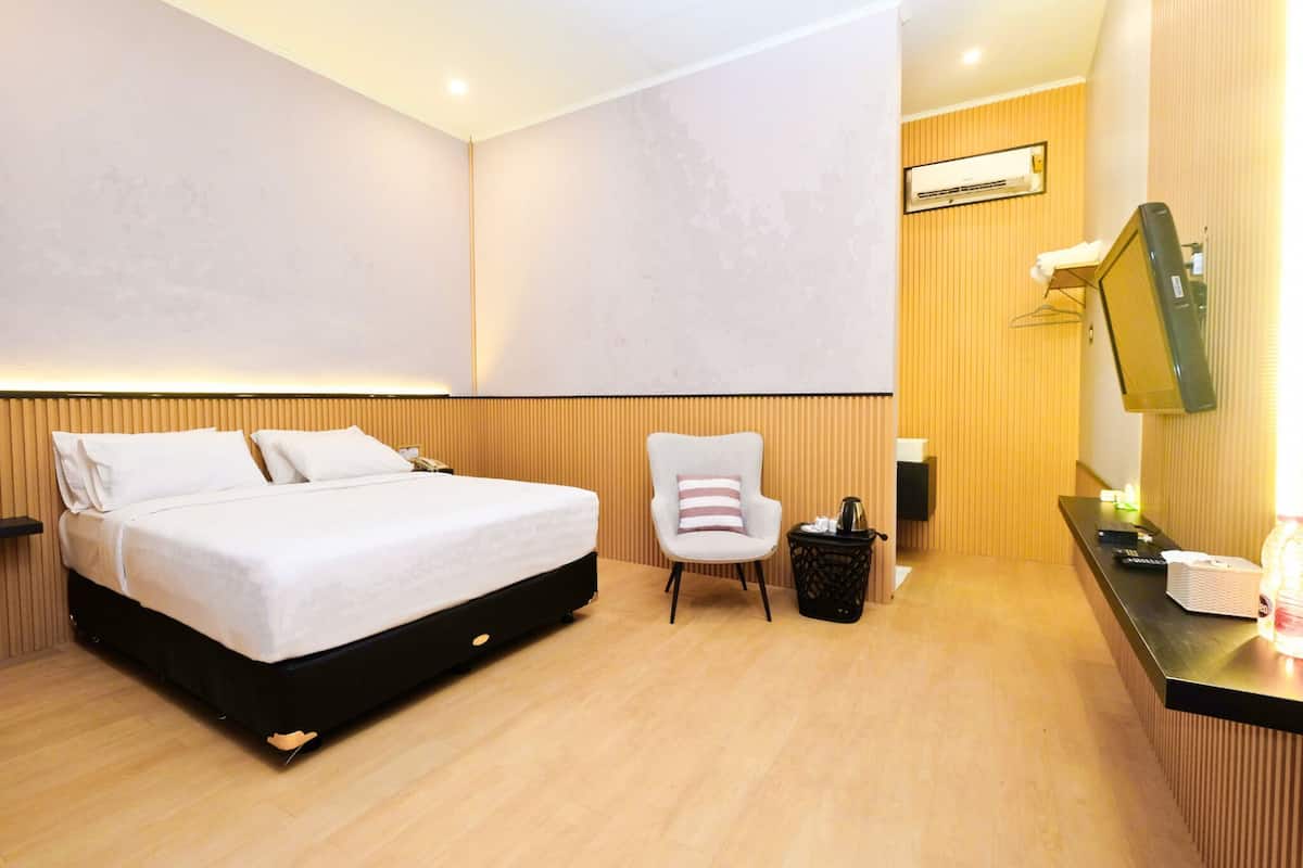 A hotel room with a bed, a chair, a desk with a computer, and a TV.