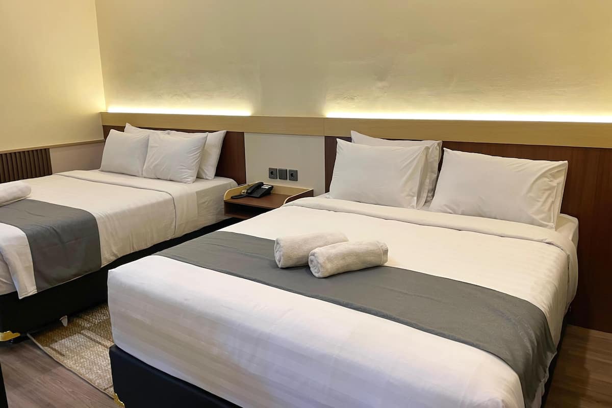 A hotel room with two beds, each with white bedding and a grey accent. There is a bedside table with a phone and a lamp.