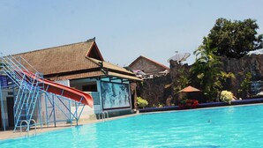 Una piscina con tobogán, un edificio de techo azulejado y un risco rocoso al fondo.