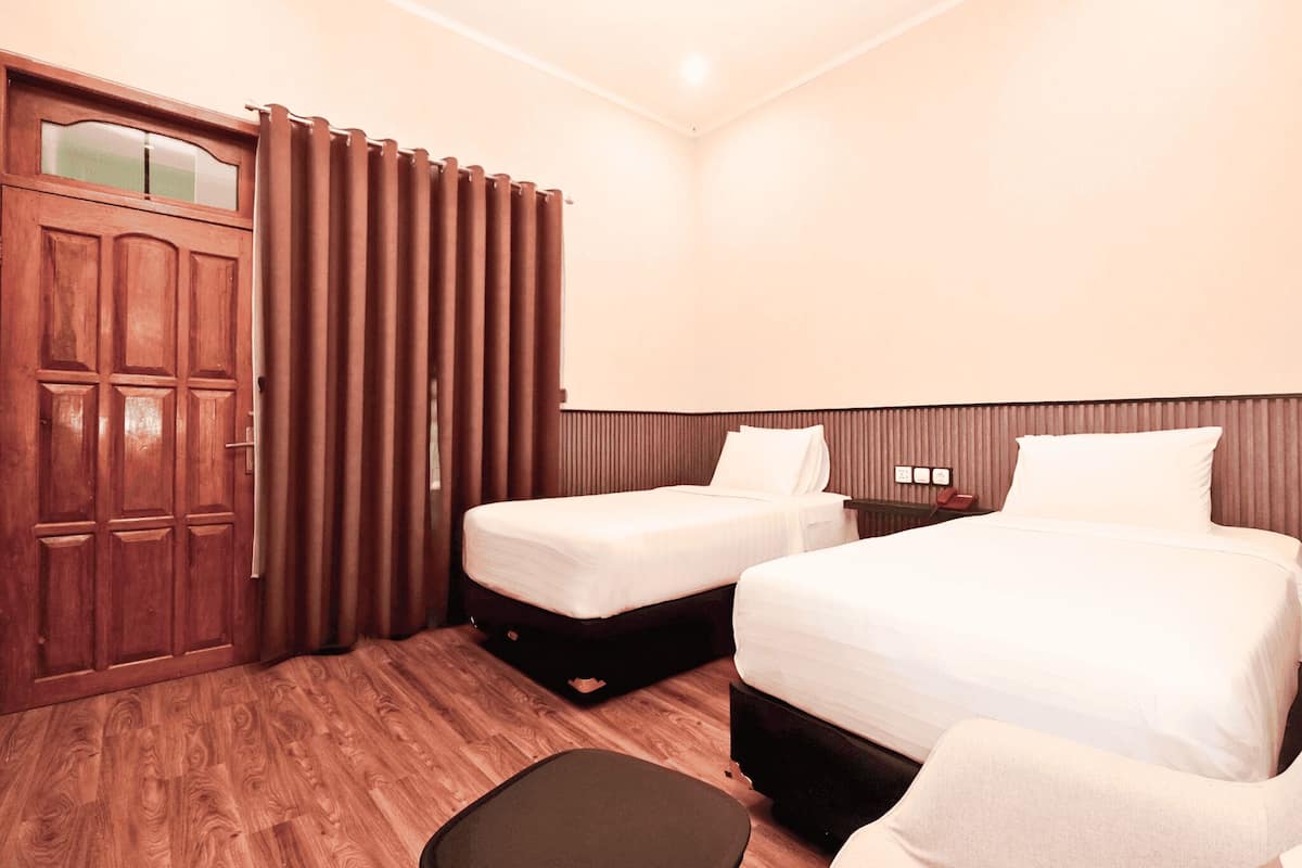 A hotel room with two beds, a wooden door, and a curtain.