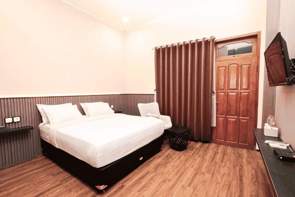 A modern hotel room with a large bed, a wooden floor, a desk with a chair, a TV mounted on the wall, and a wooden door with a window.