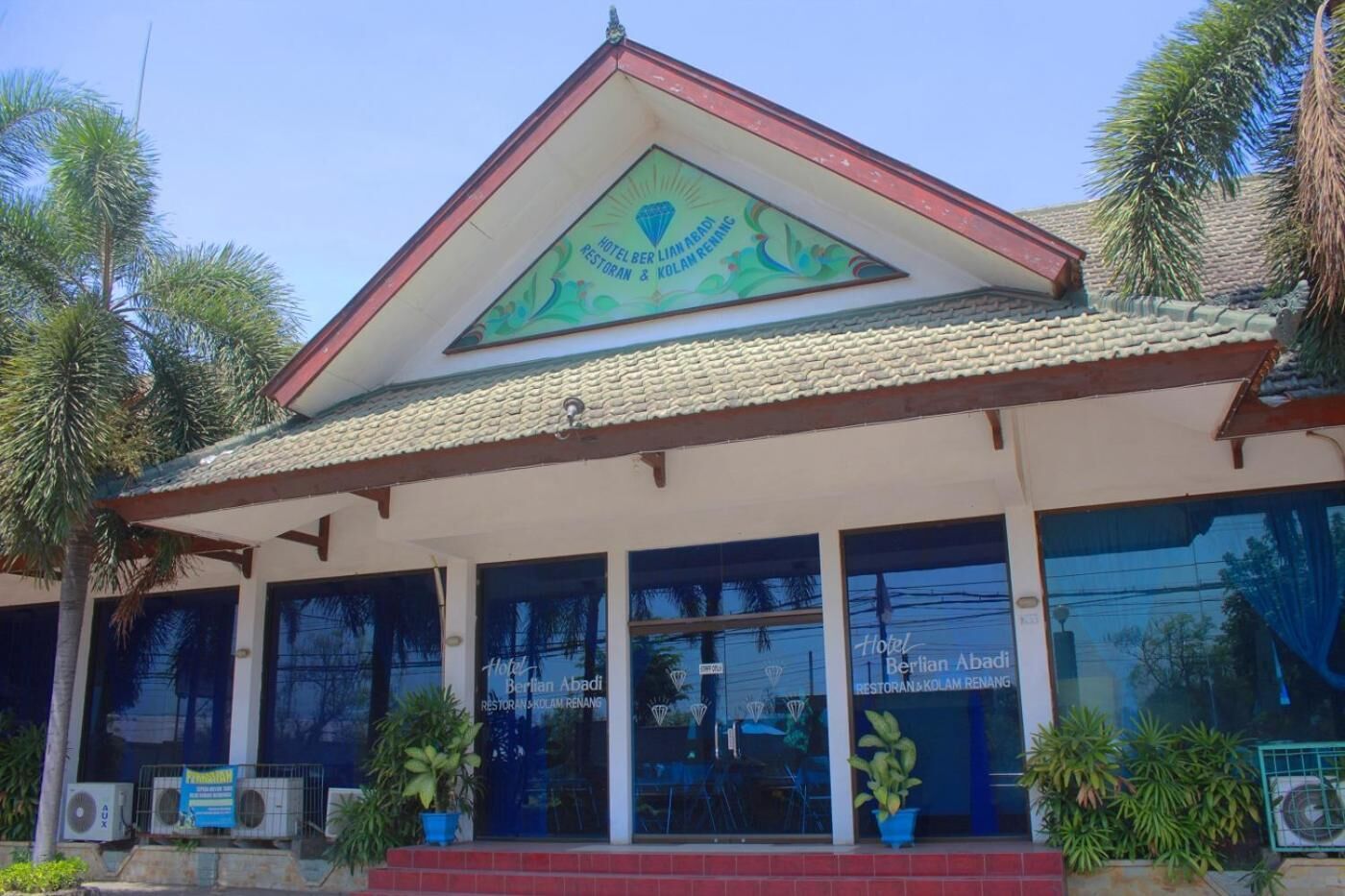 A hotel with a prominent signboard, large windows, and a tiled roof.